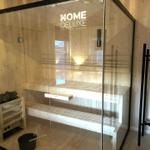 Sauna with glass enclosure and wooden bench, beside it stands a black chair.