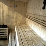 Sauna with wooden bench and stove, wall clock and light switch visible.