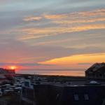 Sonnenuntergang über dem Meer mit Gebäuden und Wohnwagen im Vordergrund.