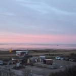 Sonnenuntergang über dem Meer mit Strand, Boot und Parkplatz im Vordergrund.