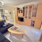 Wohnzimmer mit Sofa, Couchtisch und Holzmöbel. Küche und Schlafzimmer sind sichtbar.