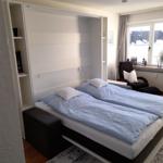 Schlafzimmer mit Bett, Sessel und Fenster. Wandbett und Regal sichtbar.