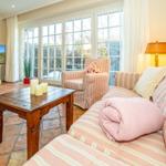 Wohnzimmer mit Sofa, Sessel, Holztisch und TV. Terrasse über große Fenster.