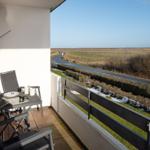 Balcony with table and chairs overlooking a road and open landscape.