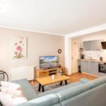 Wohnzimmer mit Sofa, Fernseher und angrenzender Küche mit Arbeitsplatten.