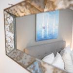 Spiegel zeigt Bett mit Kissen und Wandbild mit Segelbooten.