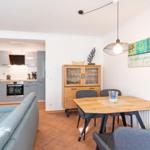 Wohnbereich mit Essbereich, Küche und Wohnzimmer. Holztisch, Sofa und Küchenschränke sichtbar.