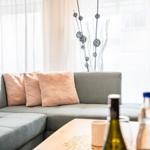 Ein Wohnbereich mit grauem Sofa, rosa Kissen und einem Holztisch mit Flaschen.