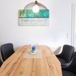 Esszimmer mit Holztisch, schwarzen Stühlen und Wandbild. Deckenleuchte über Tisch.