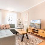 Wohnzimmer mit Sofa, TV und Holztisch. Fenster mit Vorhängen und Wandbild.