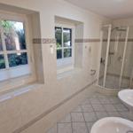 Badezimmer mit Dusche, Waschbecken und Fenstern zur Außenseite.