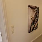 Flur mit Wandbild, Spiegel und Sicht auf Wohnbereich mit Sessel und Teppich.