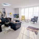 Wohnzimmer mit Ledersofa, zwei Sesseln und großem Fenster. Wandbild und Teppiche sorgen für Stil.