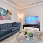 Ein Wohnzimmer mit blauem Sofa, Glas-Tisch und Fernseher auf schwarz-weißem Regal.