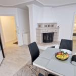 Essbereich mit Tisch, Stühlen und Kamin. Küche und Wohnbereich sind sichtbar.