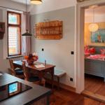 Essbereich mit Holztisch, Stühlen und Wandregal. Durchgang zu Schlafzimmer mit Bett und Wandbild.