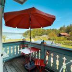 Terrasse mit rotem Sonnenschirm und Tisch. Blick auf See und grüne Landschaft.