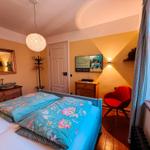 Schlafzimmer mit Bett, Fernseher, Spiegel und roter Sitzgelegenheit.