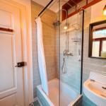 Bad mit Dusche, Waschbecken und Spiegel. Fliesen und Holzrahmen sichtbar.