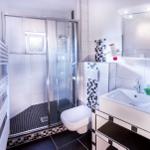 Badezimmer mit Dusche, Waschbecken und Toilette. Fliesen in Weiß und Schwarz.