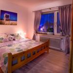 Schlafzimmer mit Holzbett, Fenster mit Vorhängen und Wandbild.