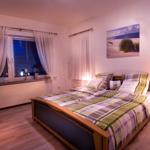 Schlafzimmer mit Bett, Nachttisch und Fenster mit Vorhängen.