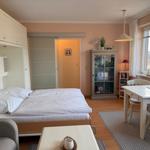 Schlafzimmer mit Bett, Tisch und Stühlen. Fenster mit Blick auf Dächer.