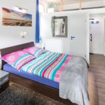 Schlafzimmer mit Doppelbett, Nachttisch und Wandbild. Holzboden und Tür zum Flur.