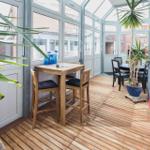 Terrassenbereich mit Holzboden, Tischen, Stühlen und Pflanzen.