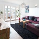 Ein Wohnzimmer mit rotem Sofa, Holztisch und Glasfront zur Terrasse.