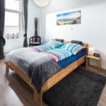 Ein Schlafzimmer mit Holzbett, Fenster, Nachttisch und Bild an der Wand.