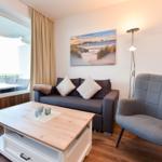 Wohnzimmer mit Sofa, Sessel, Tisch und Blick auf Balkon.