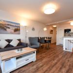 Wohnbereich mit Sofa, Couchtisch und Essbereich. Küche mit Arbeitsplatte und Treppenhaus.