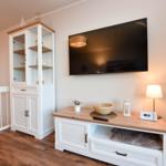 Wohnbereich mit Fernseher, Sideboard und Weinkühler. Holzboden und warme Beleuchtung.