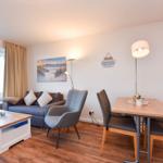 Wohn- und Essbereich mit Sofa, Stuhl, Tisch und Fenster zur Terrasse.