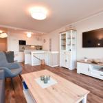 Wohnzimmer mit Fernseher, Esstisch und Küche im Hintergrund.