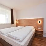 Schlafzimmer mit Doppelbett, Holzfußboden und Fenster mit Jalousie.