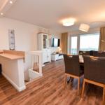 Wohn- und Essbereich mit Holzboden, Esstisch, TV und Balkontür.