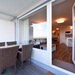 Terrasse mit Esstisch und Stühlen. Blick ins Innere mit Küche und Wohnbereich.