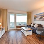 Wohnzimmer mit Sofa, Sessel, Couchtisch und Balkonzugang.