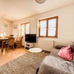 Wohn- und Essbereich mit Sofa, TV und Holztisch. Fenster mit Vorhängen.