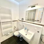 Badezimmer mit Toilette, Waschbecken und Dusche. Weiße Wände, dunkler Boden und Heizung.