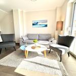 Wohnzimmer mit Sofa, zwei Sesseln und Tisch. Fenster zum Balkon. Wandbild und Stehlampe.