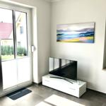 Wohnzimmer mit TV, Wandbild und Glasfront zur Terrasse.