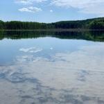 Stiller See mit Spiegelung des Himmels und Wald am Ufer.