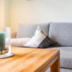 Ein grauer Sofa mit Kissen und einem Holztisch mit Kerze.