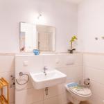 Badezimmer mit Waschbecken, Spiegel, Toilette und Heizkörper.
