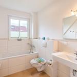 Badezimmer mit Badewanne, Toilette und Waschbecken. Fenster mit Blick auf Dach.