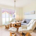 Wohnzimmer mit Sofa, zwei Sesseln und Holztisch. Durchgangstür zur Terrasse. Kaminofen.