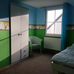 Ein Schlafzimmer mit Bett, Kleiderschrank, Stuhl und Fenster mit Vorhang.
